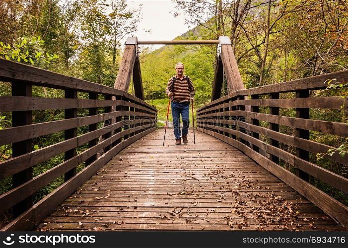 Mature man are hiking in the mountains, walking on a wooden bridge