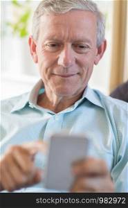 Mature Man At Home Sending Text Message On Mobile Phone