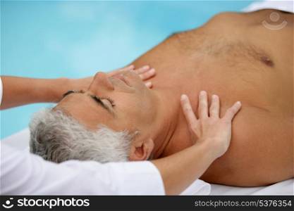 Mature man being massaged next to a swimming pool
