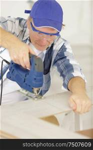 mature man carpenter working with grinder on wooden factory