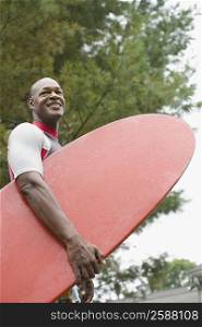 Mature man carrying a surfboard and smiling