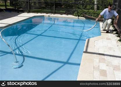 Mature man cleaning a swimming pool with a hose