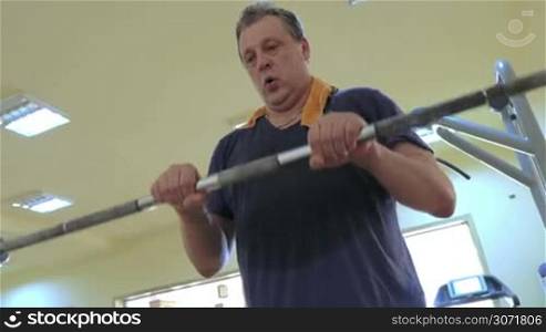 Mature man doing and finish exercise with crossbar in fitness center. He lifting it in front of himself