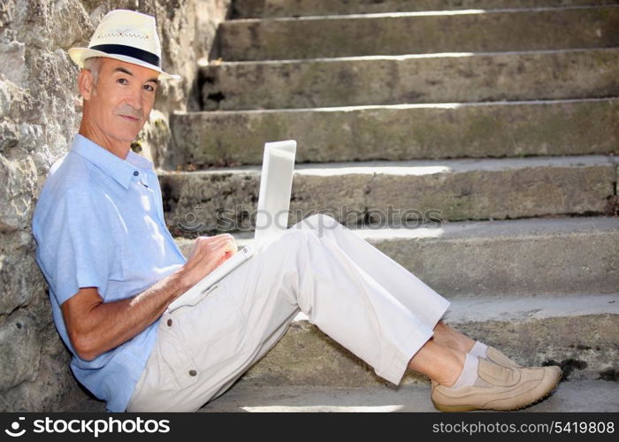 mature man doing computer outside at the foot of stairs