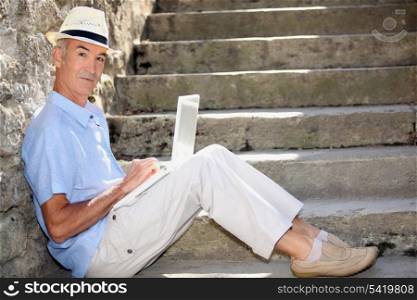 mature man doing computer outside at the foot of stairs
