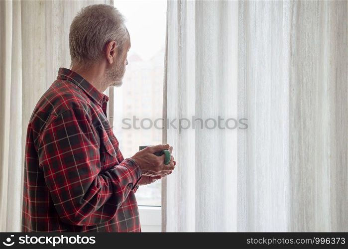 Mature man drinking his coffee in a green cup, while he is looking out of the window