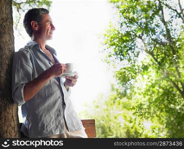 Mature man drinking tea leaning on tree looking at view profile