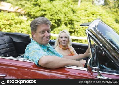 Mature man driving a convertible car with a mature woman sitting beside him
