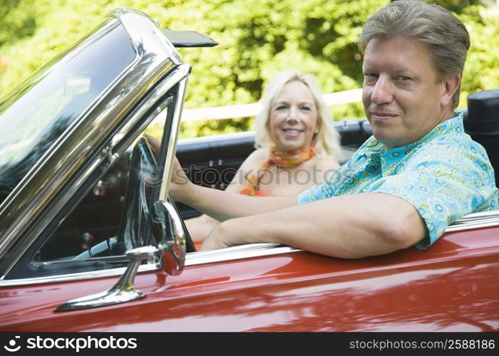 Mature man driving a convertible car with a mature woman sitting beside him