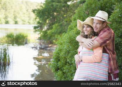 Mature man embracing a mature woman from behind near a pond