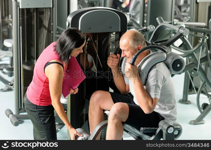 Mature man exercising at gym under supervision of personal trainer