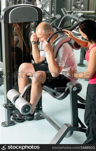 Mature man exercising at gym under supervision of personal trainer