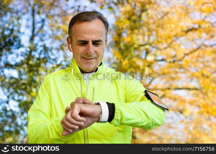 Mature Man Exercising In Autumn Woodland Looking At Activity Tracker On Smart Watch