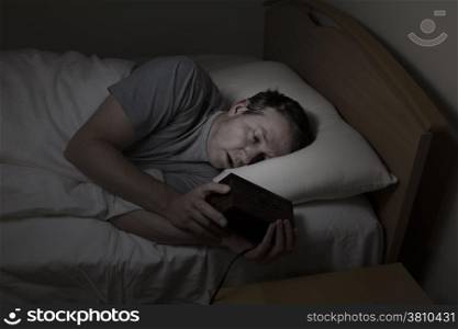 Mature man, eyes open with both hands on alarm clock while checking time, cannot sleep at night from insomnia