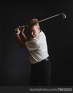 Mature man golfer wearing a white shirt and he exercise a swing - studio shot, black background