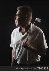 Mature man golfer wearing a white shirt and he holds a iron golf club on his shoulder and he looking away - studio shot, black background