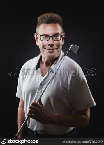 Mature man golfer wearing a white shirt and he holds a iron golf club on his shoulder and he looking at camera - studio shot, black background