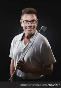 Mature man golfer wearing a white shirt and he holds a iron golf club on his shoulder and he looking at camera - studio shot, black background