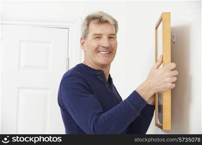 Mature Man Hanging Picture On Wall