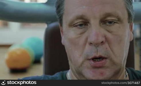 Mature man having intensive training on exercising machine in a gym. He is in a sweat and breathing deeply