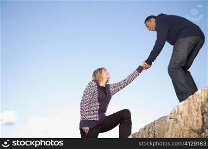 Mature man helping a mature woman to climb a rock