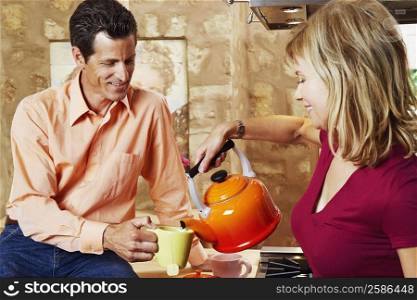 Mature man holding a cup with a mature woman pouring tea into it