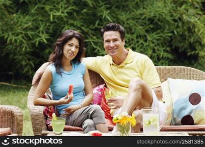 Mature man holding a glass of lemonade with a mature woman holding a slice of water melon beside him