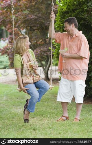 Mature man holding a glass of margarita and a mature woman sitting on a swing