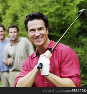 Mature man holding a golf club with his friends standing behind him