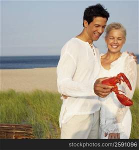 Mature man holding a lobster on the beach with a mature woman standing beside him