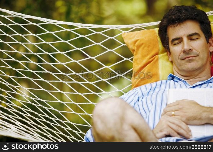 Mature man holding a magazine and sleeping in a hammock