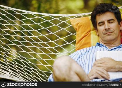 Mature man holding a magazine and sleeping in a hammock