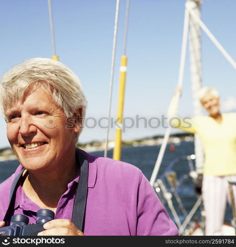 Mature man holding a pair of binoculars in a boat with a mature woman standing behind him