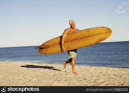 Mature man holding a surfboard and walking on the beach