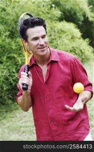 Mature man holding a tennis racket and tossing a tennis ball