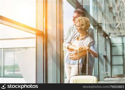 Mature man hugging his wife from behind while looking through the window in airport