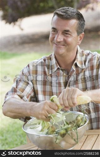 Mature man husking a corn over a bowl