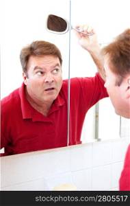 Mature man in his forties uses a mirror to check for bald patches in his hair.