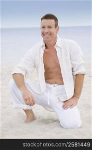 Mature man kneeling on the beach and smiling