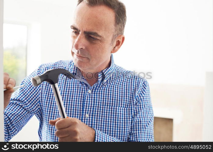 Mature Man Knocking Nail Into Wall With Hammer