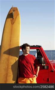 Mature man leaning against a sports utility vehicle with a surfboard