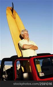 Mature man leaning against a surfboard in a sports utility vehicle