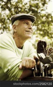 Mature man leaning on a golf bag and smiling
