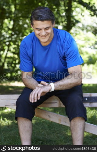 Mature Man Looking At Activity Tracker Whilst Exercising In Countryside