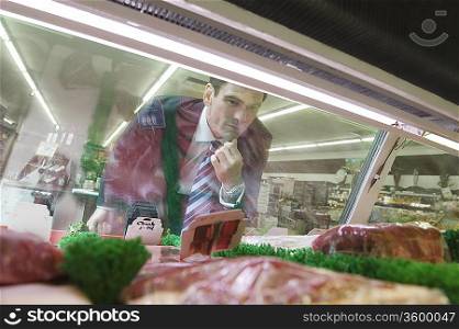 Mature man looks through glass of meat counter in supermarket
