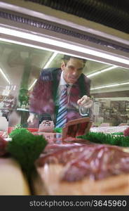 Mature man looks through glass of meat counter in supermarket