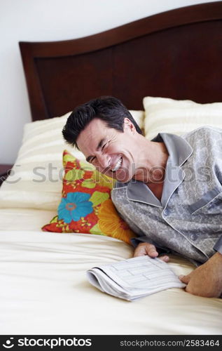 Mature man lying on the bed and holding a newspaper