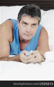 Mature man lying on the bed and operating a remote control