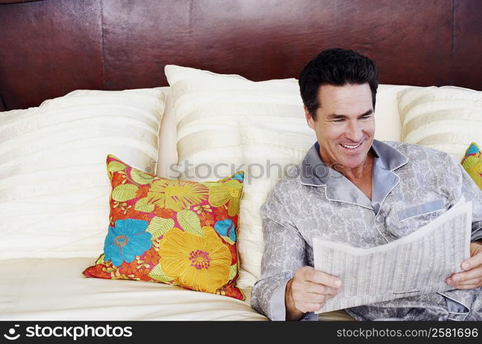 Mature man lying on the bed and reading a newspaper