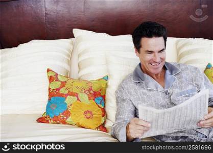 Mature man lying on the bed and reading a newspaper